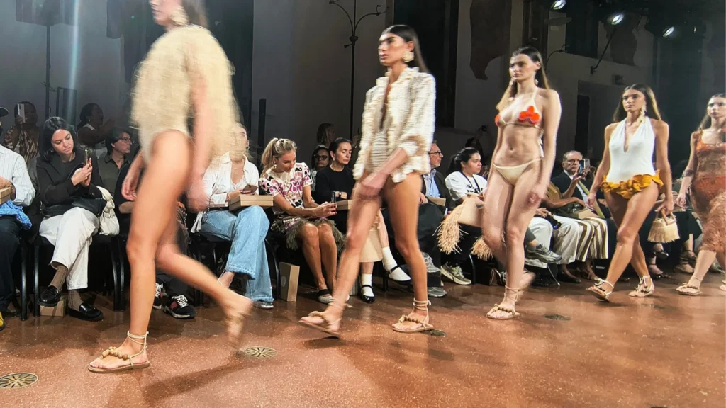 Sfilata di moda sostenibile brasiliana alla Milano Fashion Week nei Chiostri di San Barnaba con modelle in passerella con abiti e accessori in fibre naturali.