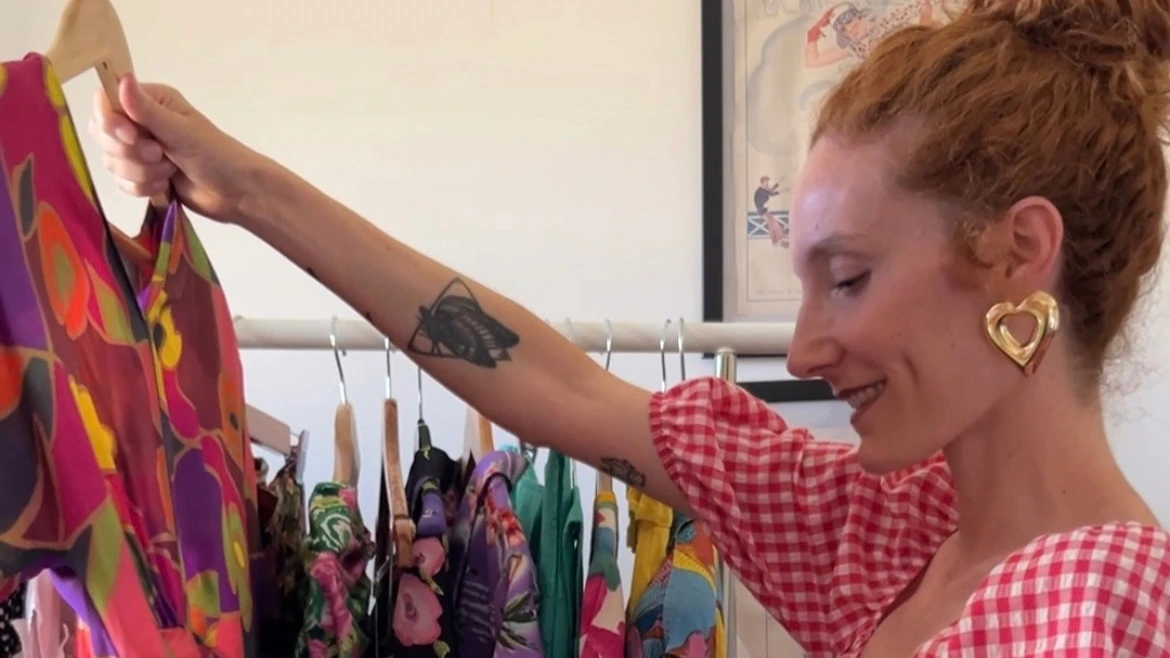 Annalisa Fortunato di Curly Vintage sorride mentre mostra un abito colorato a fantasia su uno stender di abiti second hand