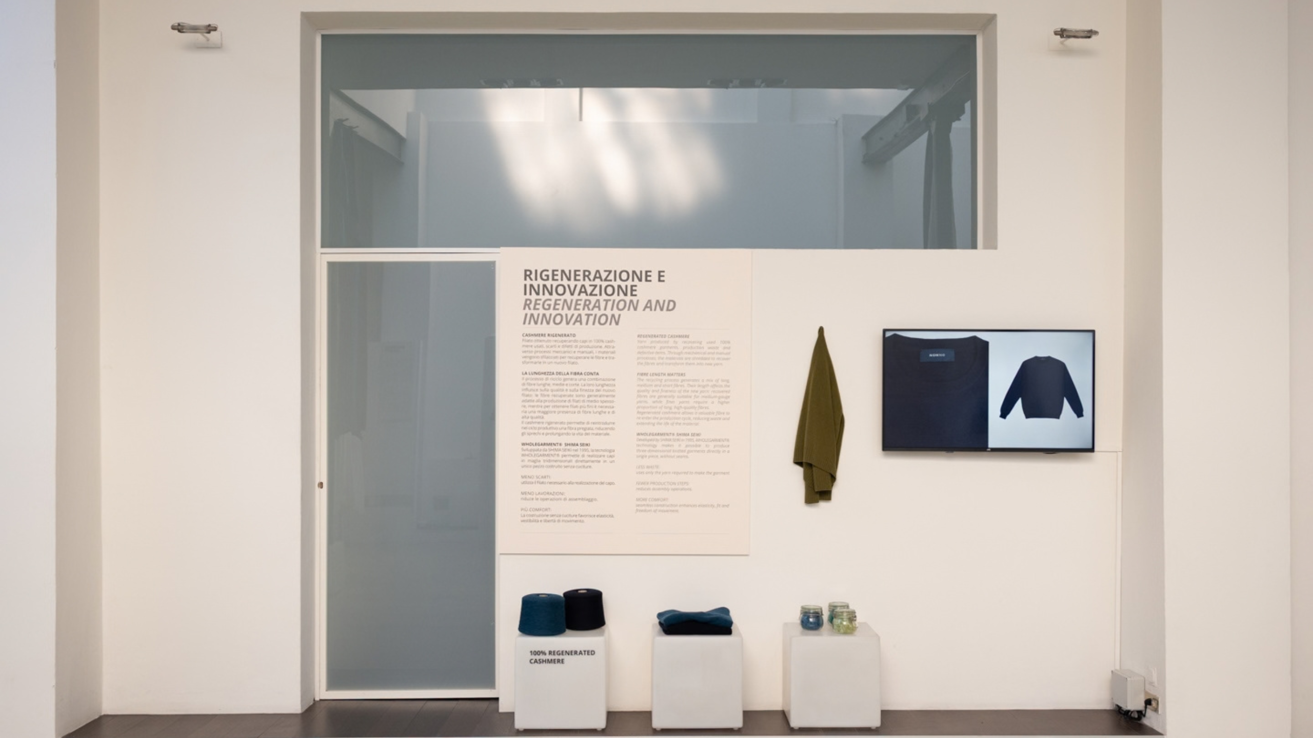Pannello illustrativo sulla rigenerazione e innovazione tessile con rocchette di filato e uno schermo espositivo alla mostra MATTER MATTERS. Foto di Luigi Colonna.