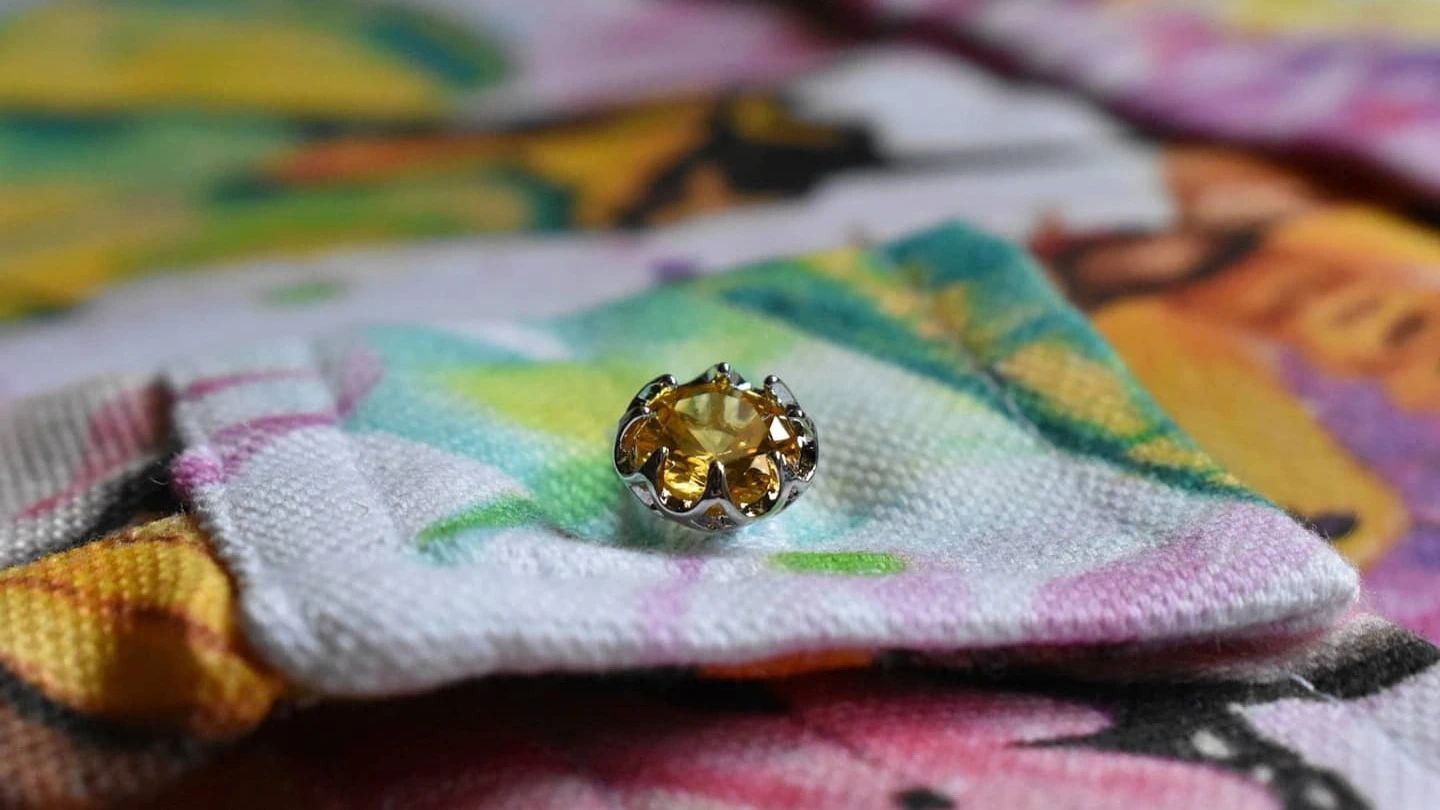 Dettaglio ravvicinato di un bottone gioiello punto luce incastonato su polsino in tessuto d'arredo di una camicia Michele Roncada